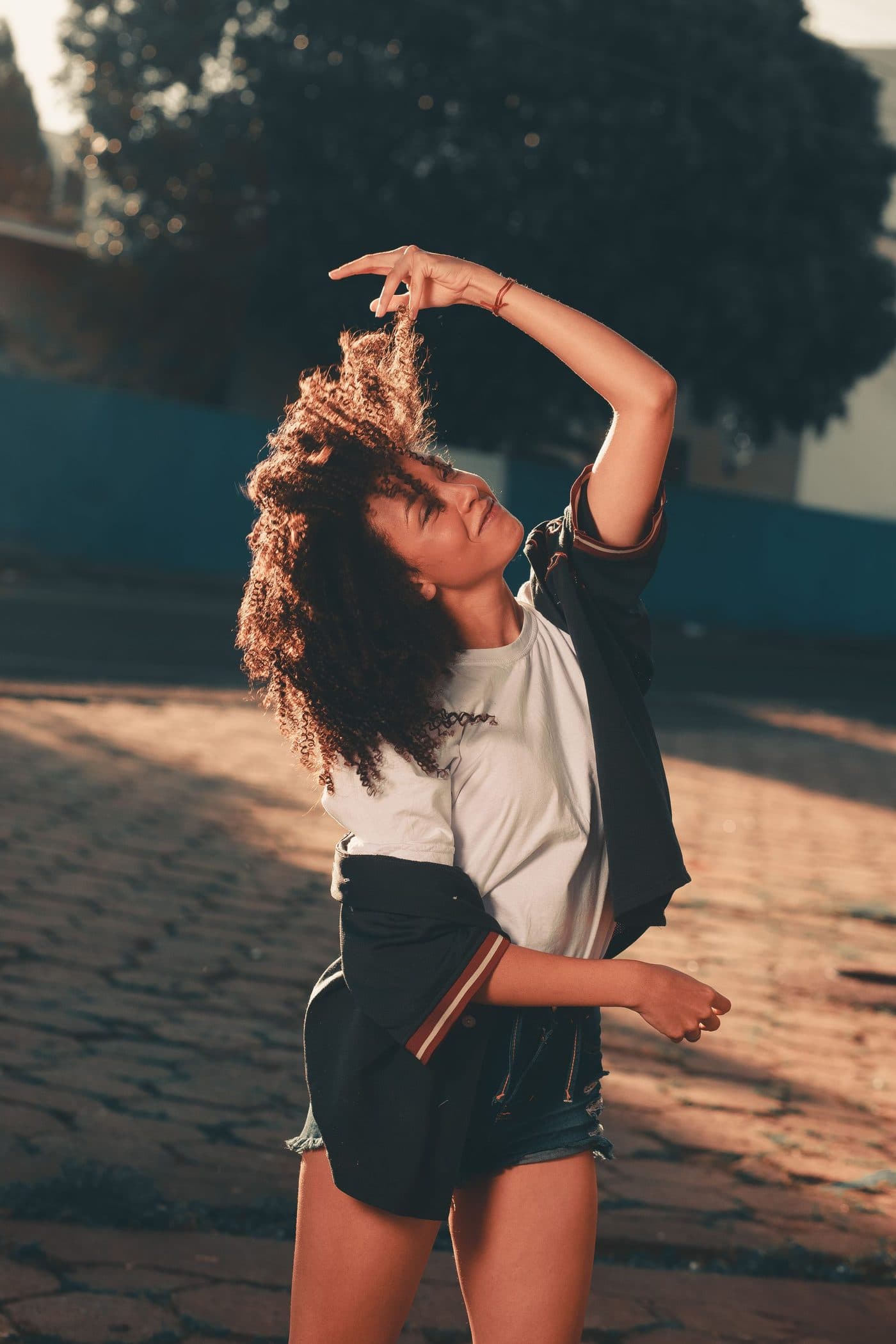 Danseuse en plein mouvement afro & reggaeton, bras levé, sous une lumière dorée