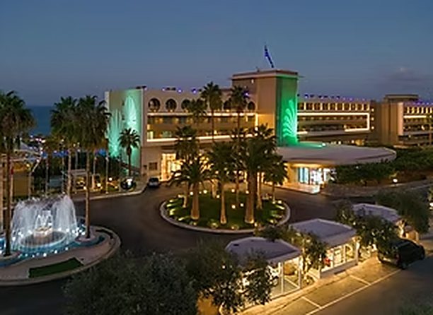 Façade illuminée de l’hôtel, palmiers et fontaine en soirée