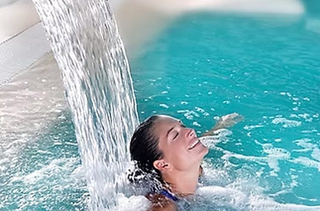 Smiling woman under a waterfall in a pool